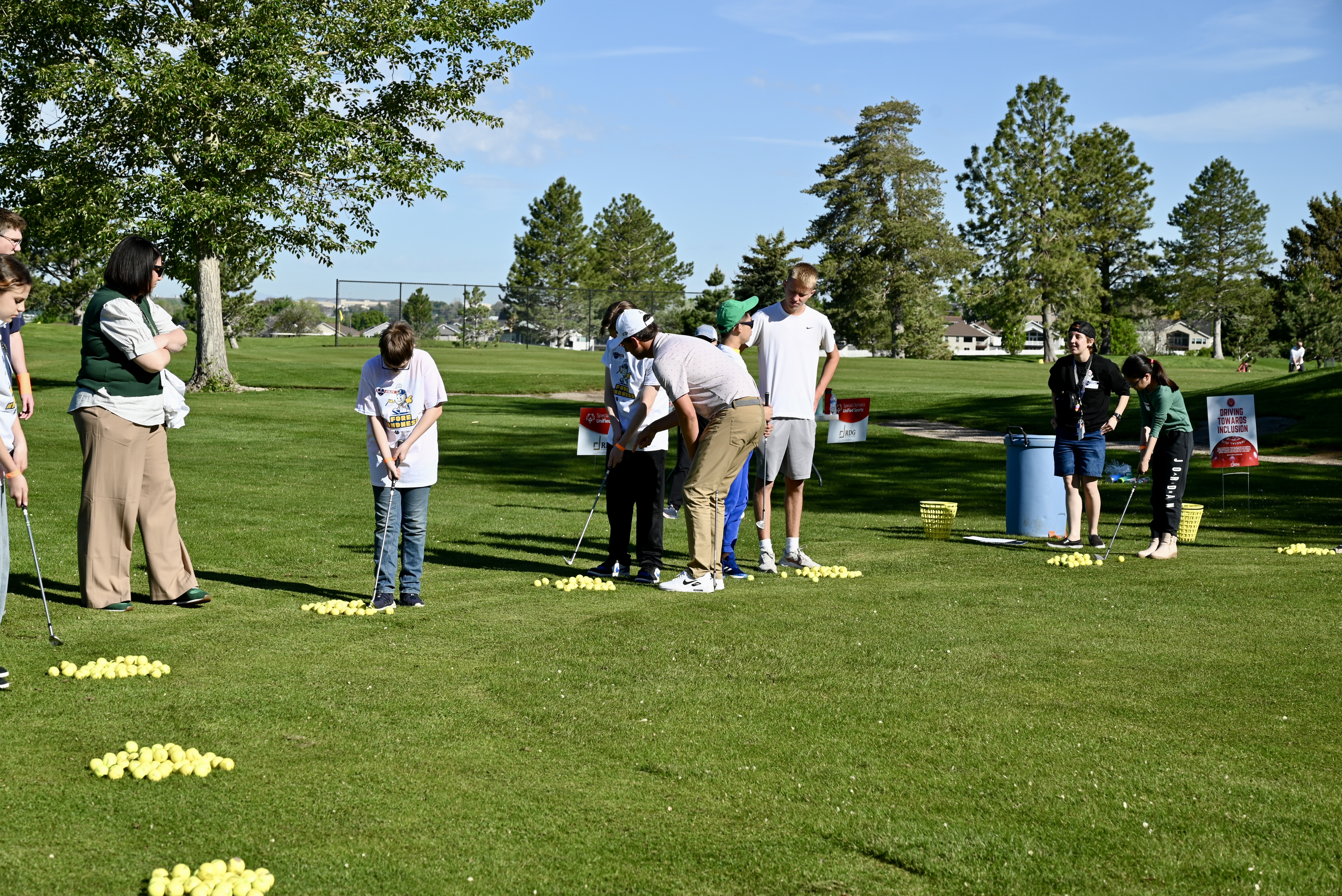 Group driving range lesson with yellow practice balls scattered on the ground