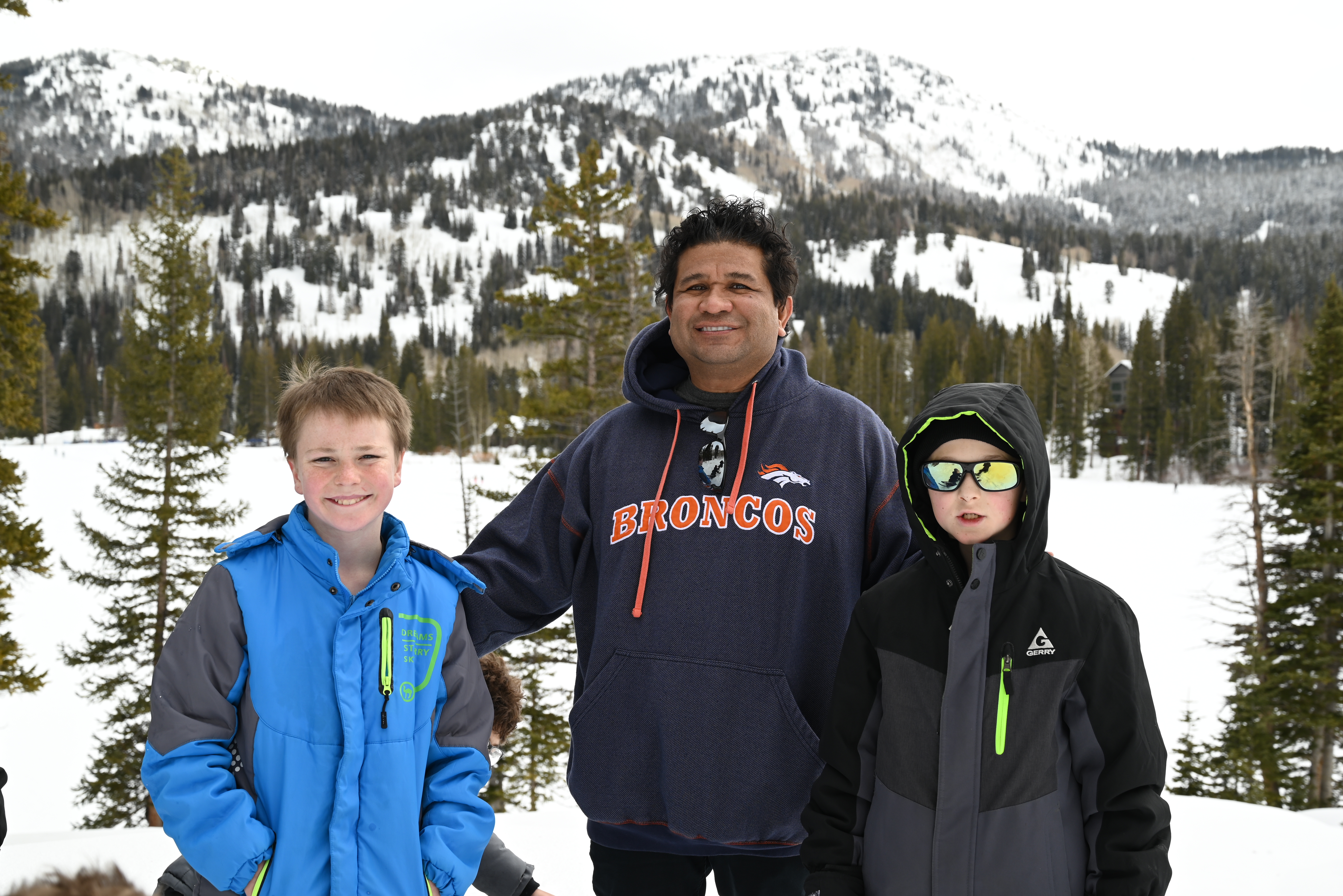 An adult and two boys posing together with a snowy mountain backdrop