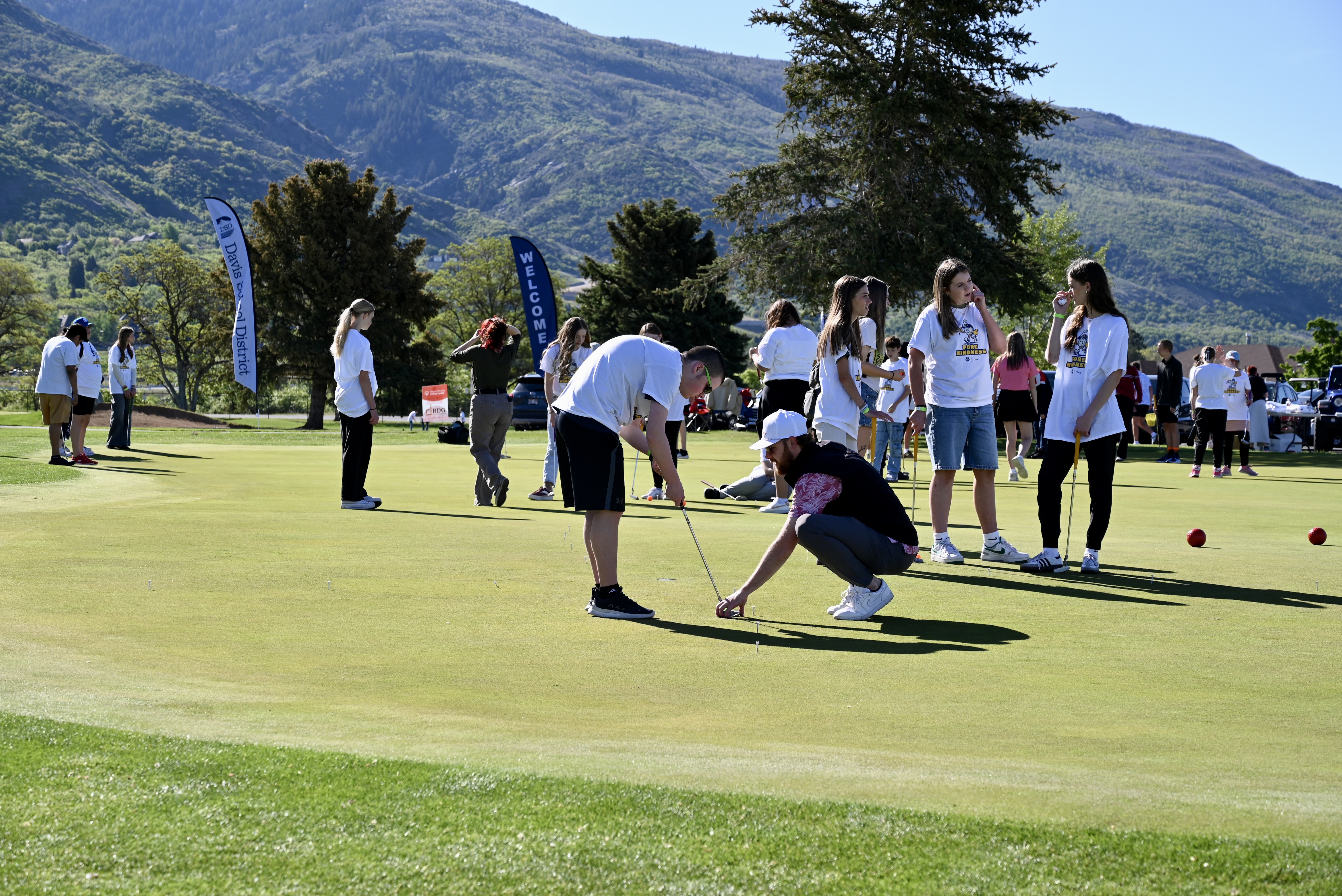 Students practicing putting with mountain views and event banners in the background